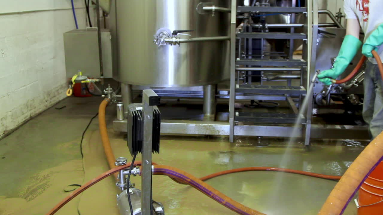 trabajador de la fábrica de cerveza limpiando el suelo del almacén con agua