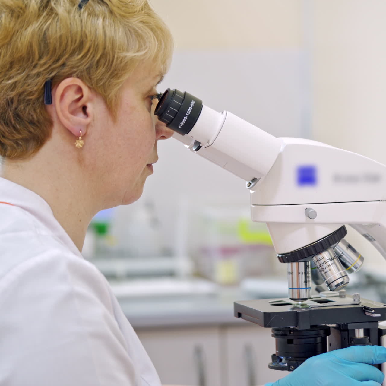 Scientist female is looking through microscope in modern laboratory. Side view of a doctor analyzing blood sample in a microscope in medical center.