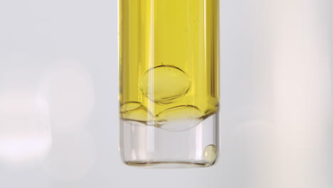 air bubbles dropping to the bottom of a test tube in an oily yellow liquid