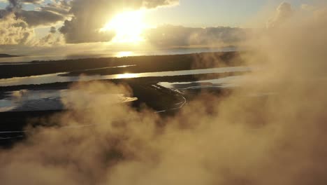 drone shot revealing coal and metal factory at sunrise, flying through large steam smoke stacks in operation