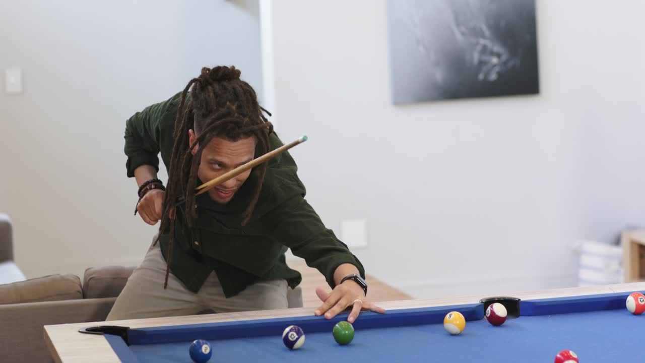 Man entering game room carrying cue stick, aligning, striking cue ball to scatter balls on table
