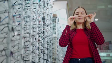 lovely girl choosing eyeglasses in the store. beautiful young woman trying on stylish transparent glasses and smiling on camera indoors.