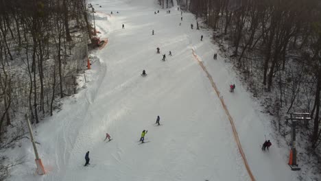 skiers and snowboarders skiing on snow slopes with ski lift at weekend. drone flying over snowy slope with skiers and snowboarders at ski resort on a frosty winter day: drone view