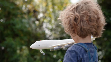 little boy playing with toy airplane happy child playing game imagining travel freedom having fun outdoors in sunny park enjoying childhood 4k