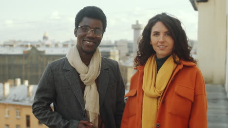 portrait of smiling multiethnic man and woman on rooftop terrace