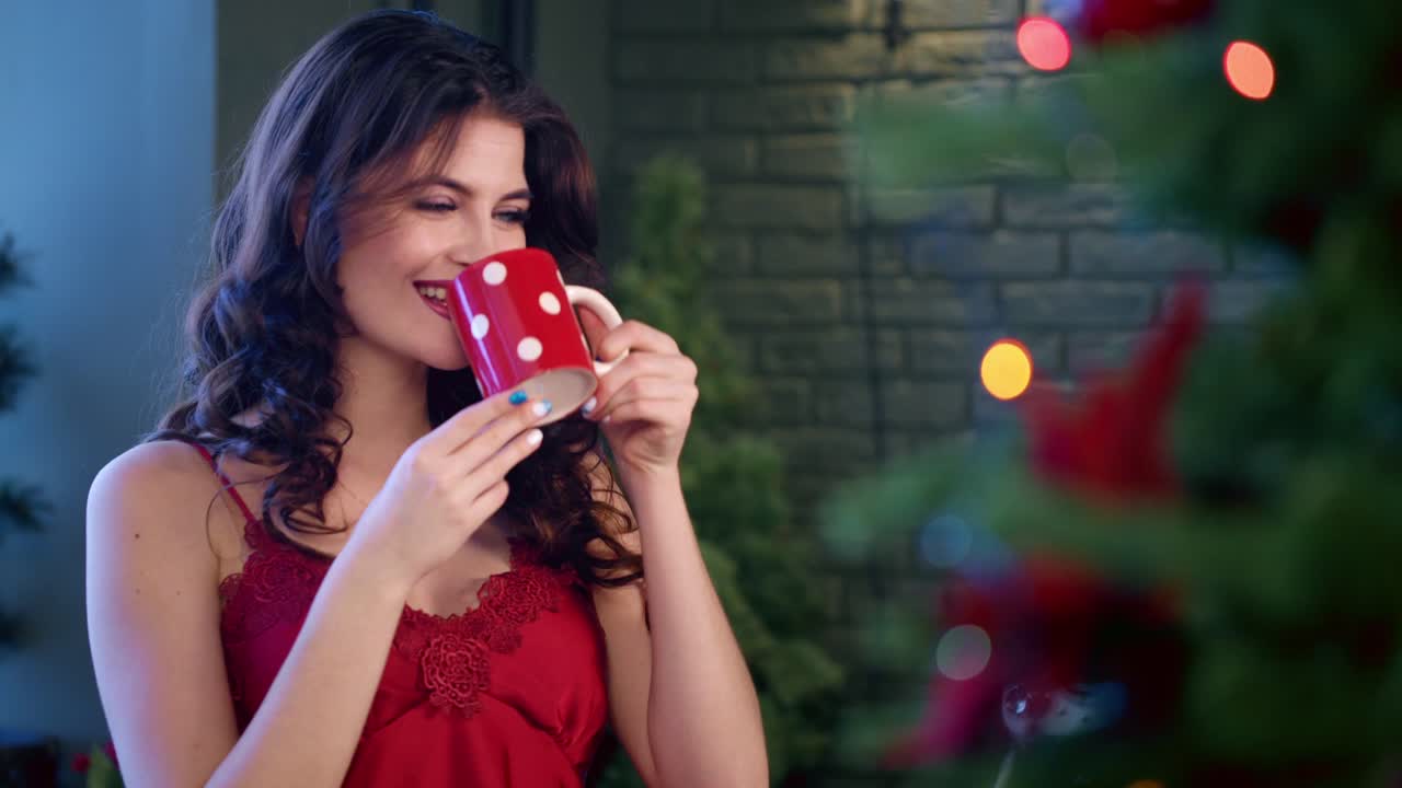 Enchanting Winter Moments: A Young Woman Savoring Her Warm Beverage by the Christmas Tree, Capturing the Joy of the Festive Season in Every Sip and Smile