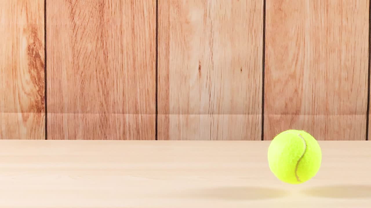 A yellow tennis ball bounces repeatedly on a smooth wooden floor against a wooden panel background.