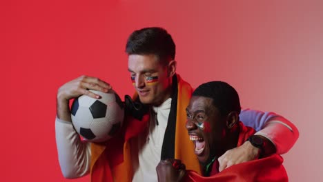 vielfältige glückliche männliche fußballfans mit nationalen fahnen über rosa beleuchtung