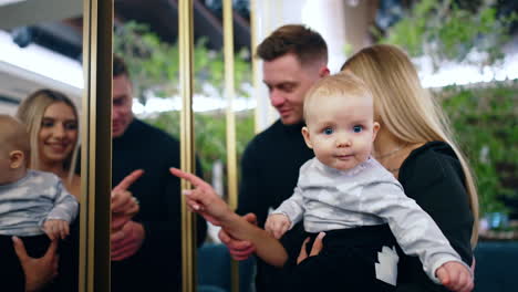 caring caucasian parents with their beloved infant baby. mom holds the baby boy showing him the mirror but kid looks at camera.