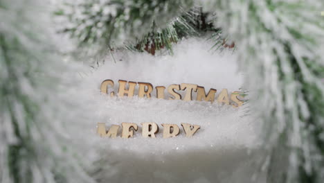 Merry-Christmas-greetings,-wooden-letters-in-snowy-pine-tree-forest-on-a-Sunny-Winter-day