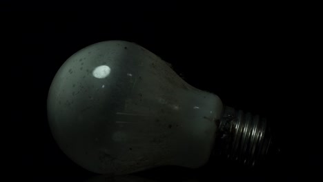 lámpara de tungsteno incandescente cubierta de polvo que refleja una bombilla incandescente sobre fondo negro