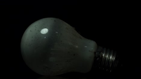 dust-covered incandescent tungsten lamp reflecting glowing light bulb on black background