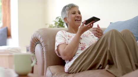 Feliz-Mujer-Birracial-Mayor-Sentada-En-El-Sofá-Y-Hablando-Por-Teléfono-Inteligente-En-Casa,-Cámara-Lenta