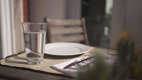 sauberes wasser in ein glas gegossen, das am tisch gelegt wird, mittagessen zu hause, nahaufnahme