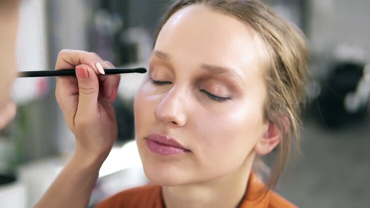 Overview of a make up process. Professional make up artist gently putting nude eyeshadows on and eyelid. Attractive young blonde
