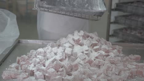un trabajador de una fábrica vuelca una bandeja grande de cuadrados de delicias turcas terminados sobre una mesa para empacar