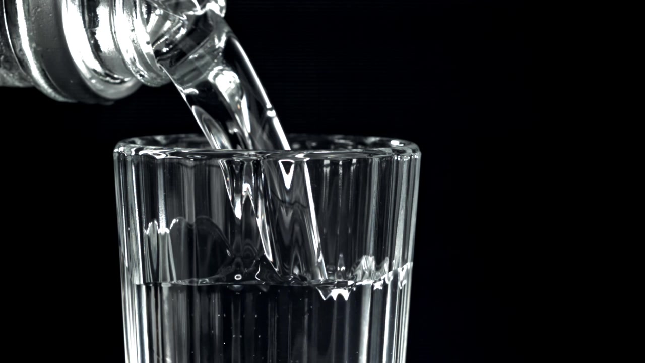 Klart vand hældes fra flaske i glas i slow motion