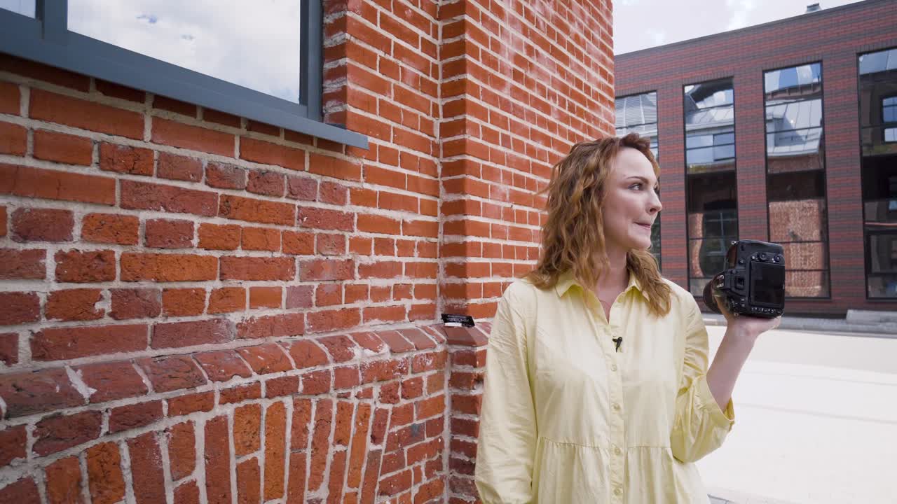 벽돌 벽 앞 에 카메라 를 들고 있는 여자 사진작가