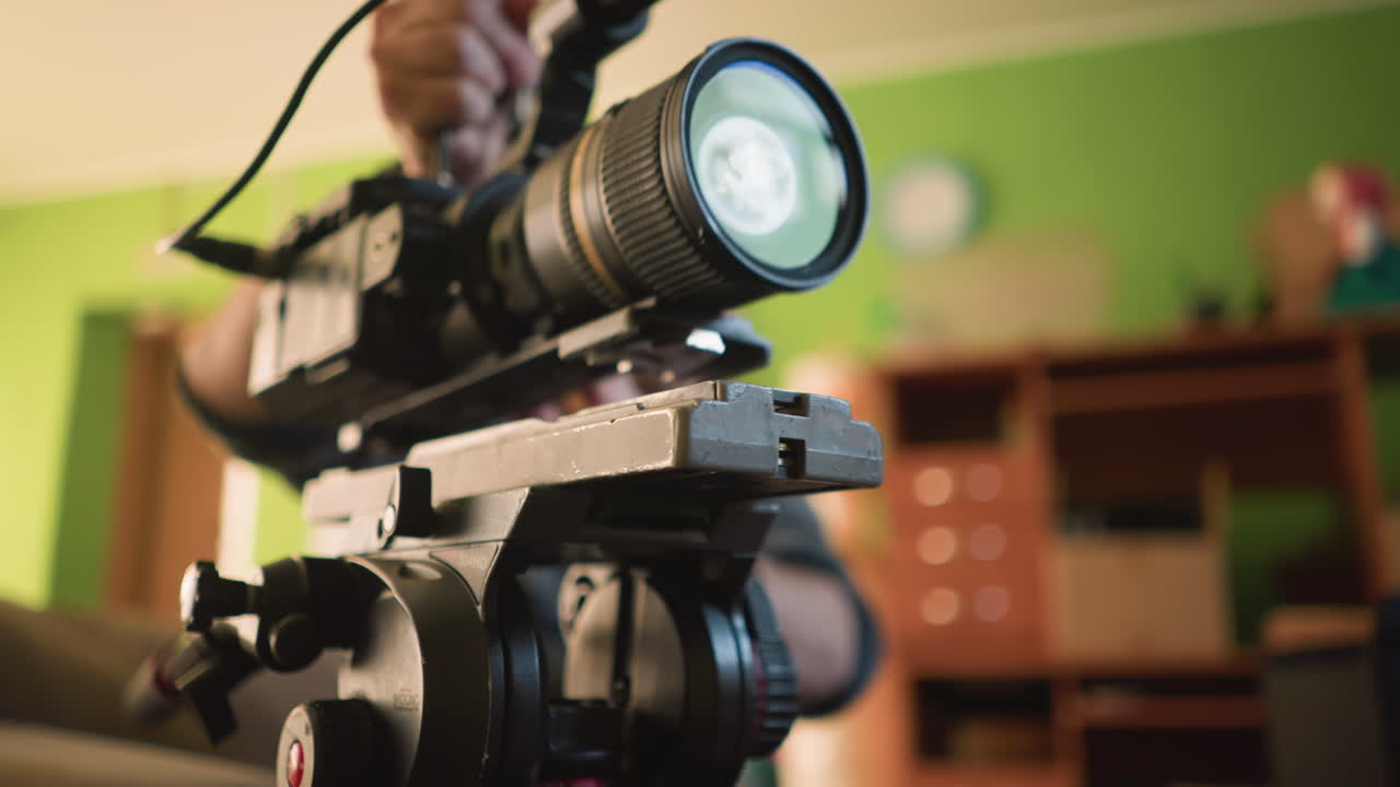Broadcast director focusing on camera and microphone setup, preparing for video shoot in home studio. Camera gear and accessories on table, getting ready for production
