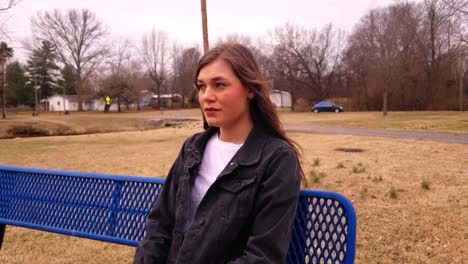 imágenes en 4k de una hermosa adolescente universitaria morena sentada en un banco de un parque de la ciudad mirando a lo lejos perdida en su pensamiento mientras su cabello ondea con el viento