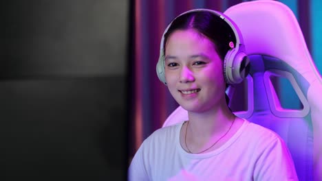close up of asian teen girl gamer smiling to camera while playing video game on computer