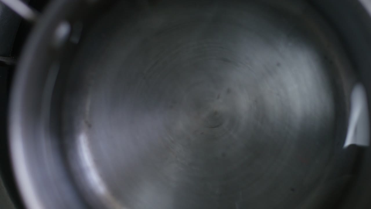 A closeup top view of putting a metal pot filled with water on a stovetop