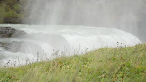 distant shot of green grass waving in a field with a magestic waterfall in the background