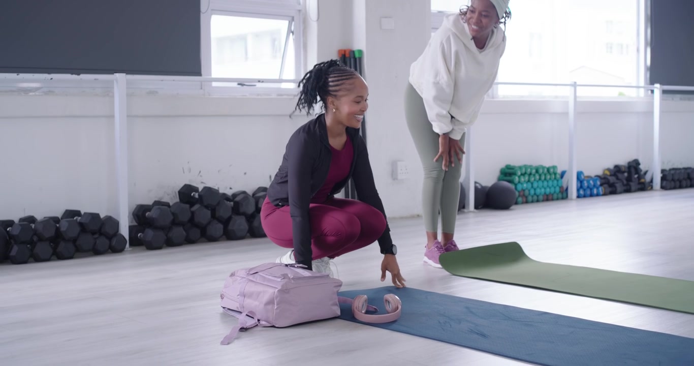 African women arriving in yoga studio, unrolling mats, placing bags and bottle, preparing workout
