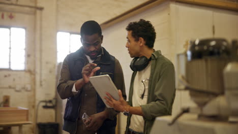 Two men discussing woodworking plans on a tablet in a workshop