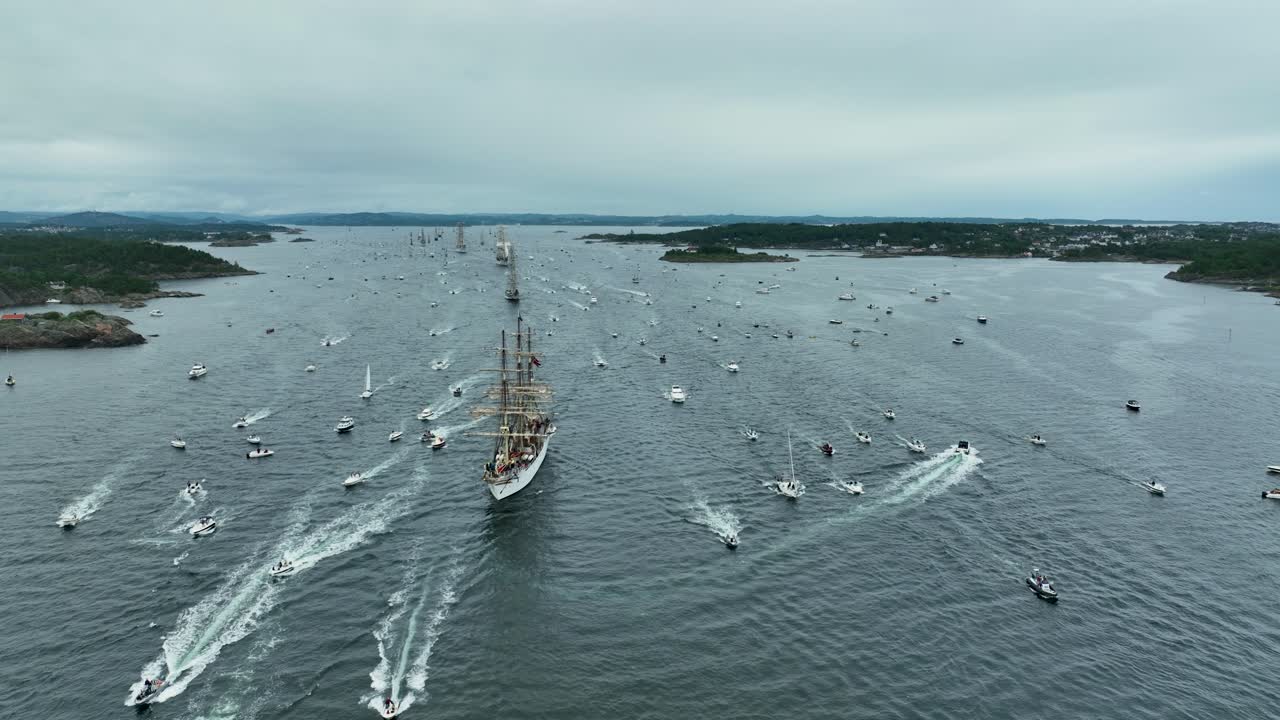 Countless boats and sailing ships fill the bay as they participate in a maritime festival. The overcast skies set a dramatic backdrop for this lively waterway event