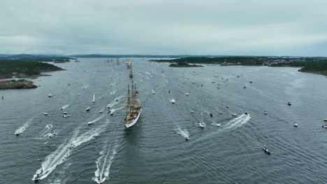 countless boats and sailing ships fill the bay as they participate in a maritime festival. the overcast skies set a dramatic backdrop for this lively waterway event