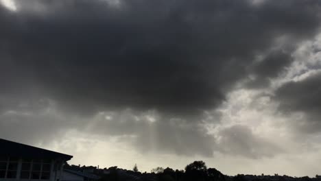 Dark-grey-ominous-clouds-with-sun-rays-beaming-through-over-the-cityscape