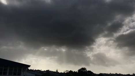 nubes ominosas de color gris oscuro con rayos de sol resplandeciendo sobre el paisaje urbano