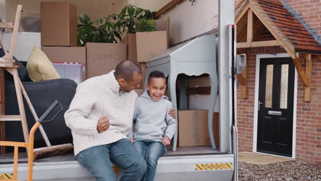 Portrait-Of-Father-And-Son-Sitting-On-Tailgate-Of-Removal-Truck-On-Moving-Day