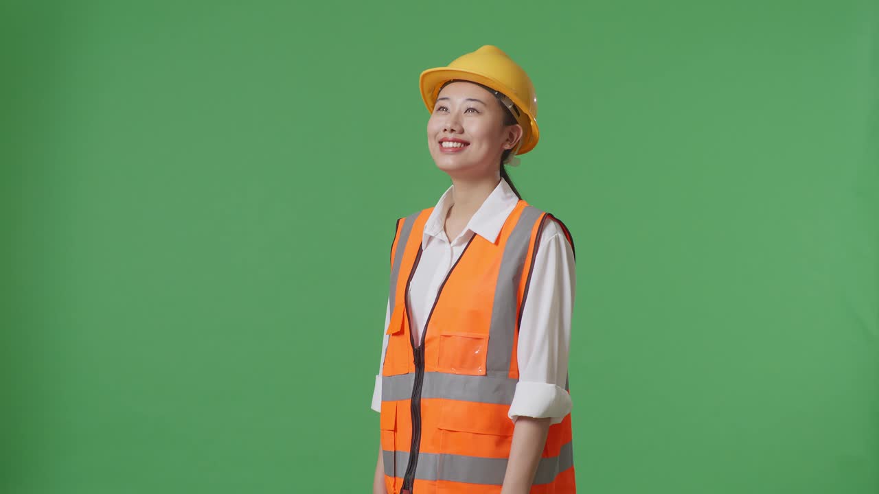 Side View Of Asian Female Engineer With Safety Helmet Looking Around While Standing In The Green Screen Background Studio