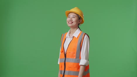 side view of asian female engineer with safety helmet looking around while standing in the green screen background studio