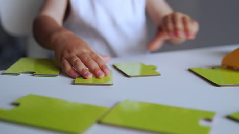 little hands of unrecognized baby playing with puzzles. kid moves the pieces trying to connect them properly. close up.