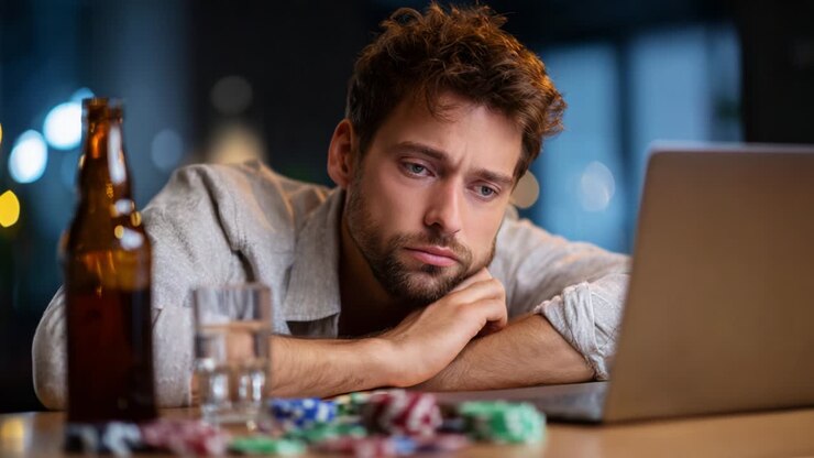 A contemplative man gazes at his laptop screen, reflecting deeply on his situation. Surrounded by poker chips and a glass of water, he tunes out distractions, lost in thought about gaming decisions