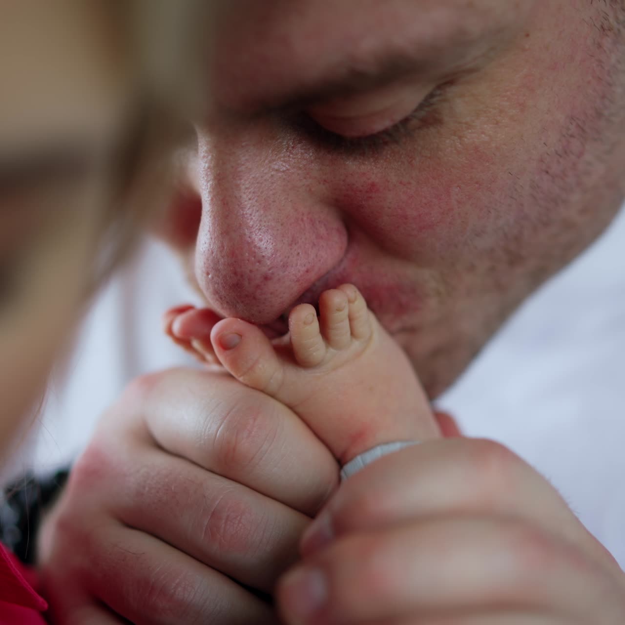 Happy parents kissing their newborn baby. Father's hand holding tiny infant's bare feet and kissing them. Close up
