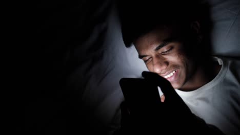 young man using phone in bed at night