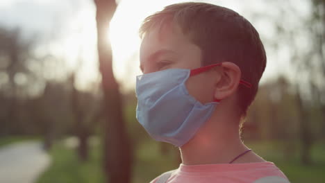 Young-guy-standing-in-medical-mask-outdoors.-Teen-boy-caring-from-coronavirus.