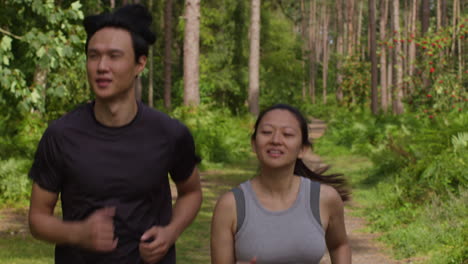 mid adult couple exercising doing work out outdoors running along track through forest towards camera wearing sports clothing 3