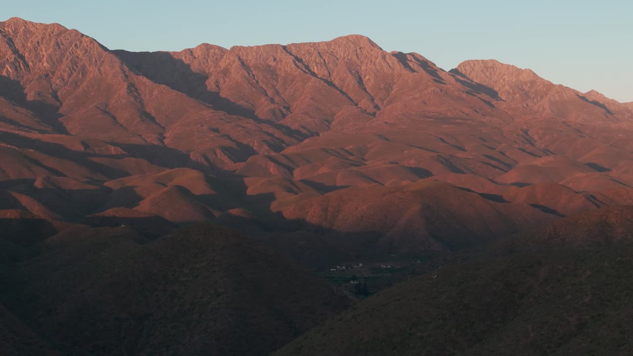 fotografía aérea de las impresionantes montañas rojas de karoo, cabo occidental, sudáfrica, al atardecer. la luz dorada destaca los vibrantes tonos rojos de los picos, creando una escena impresionante y dramática.