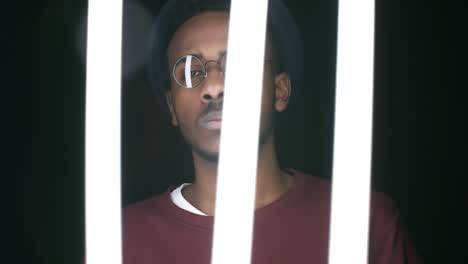 black man posing behind swinging fluorescent lamps