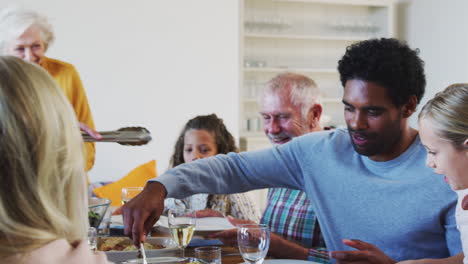 multi-generation family enjoying meal sitting around table at home together