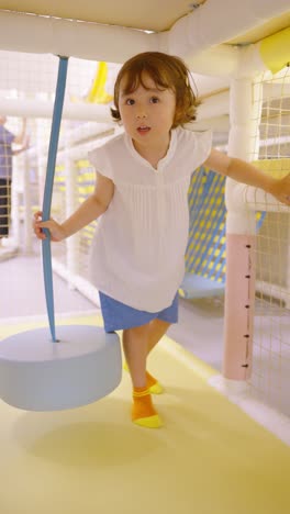 five-year-old girl happily rides on a soft swing in a bright indoor playground
