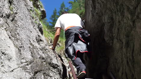 a young man climbing up a steep and narrow way going to the rocky mountains on a sunny day - close up shot