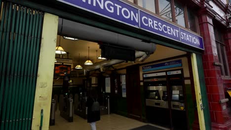 woman in casual attire taps card to enter mornington crescent station at dusk. london, uk