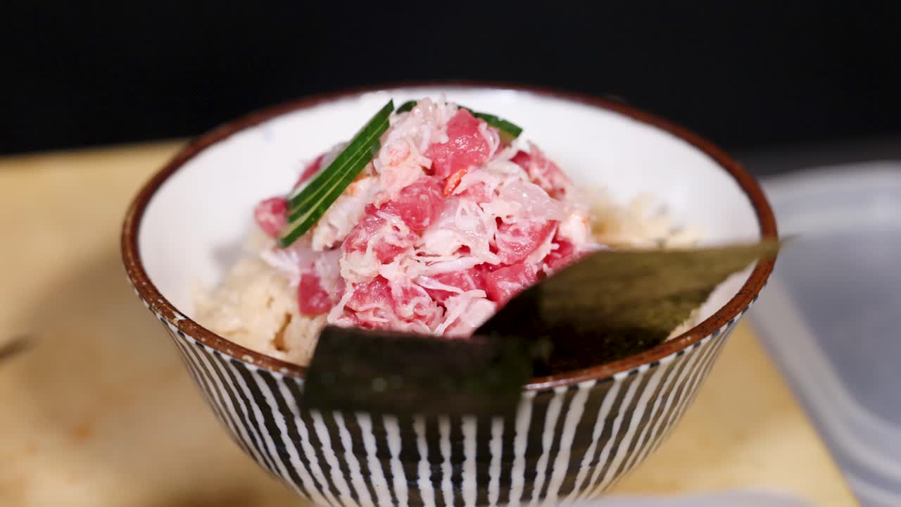 Close-up shot of a chef's hands placing cucumber slices on a crab and tuna bowl
