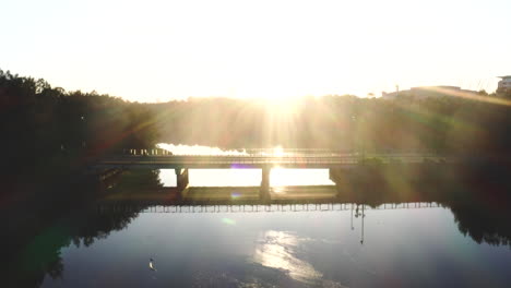 a motorbike rides across a bridge over the water silhouetted by the sunrise behind